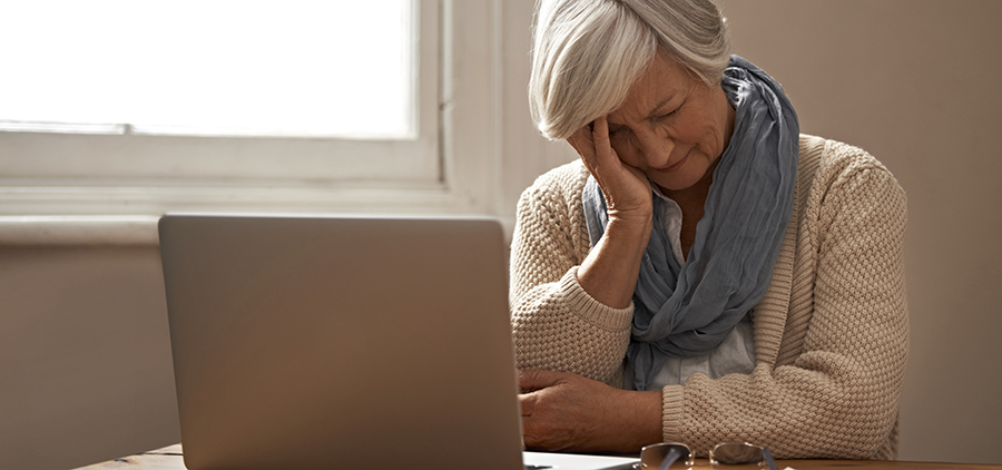 An elderly woman sitting in front of her laptop looking stressed and worried
