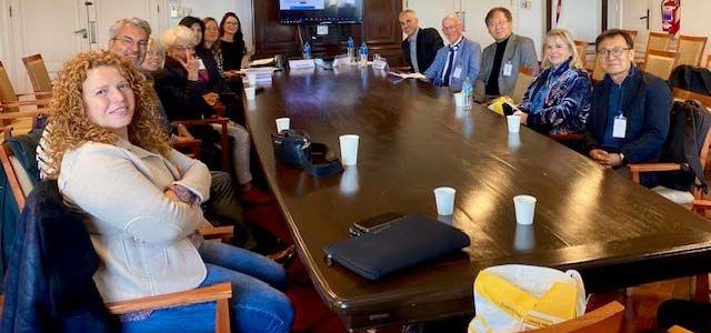 Group of about six professionals smile at the camera around a board table.